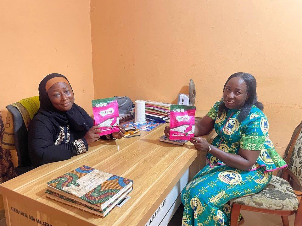 Two women holding packs of sanitary pads at a handover meeting