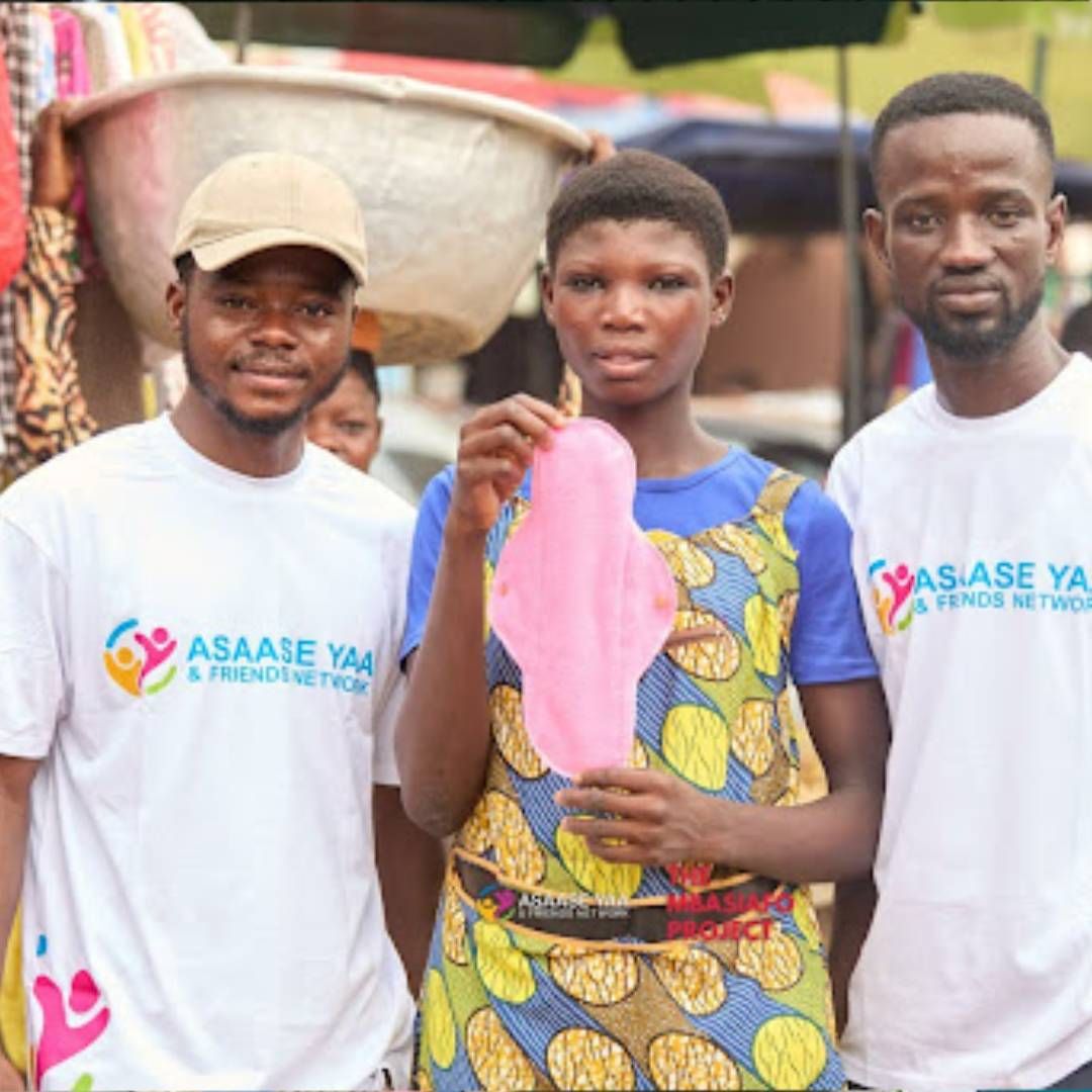 Young woman holding a reusable sanitary pad with two Asaase Yaa volunteers
